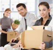 A professional woman and man storing office supplies and documents into a cardboard box in a modern office setting.