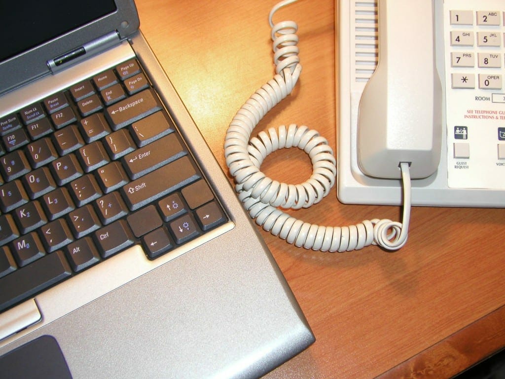 A laptop connected to a telephone via a coiled cable, storing data on a wooden desk.