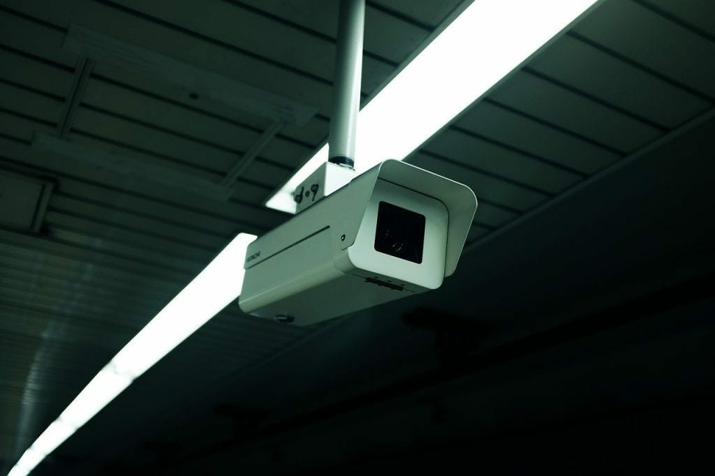 Security camera mounted on a ceiling with fluorescent lights in a dimly lit self storage room.