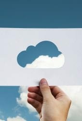 A hand holding up a piece of paper with a cloud-shaped cutout, aligning the cutout with a real cloud in a blue sky, symbolizing creative storing of visual elements.