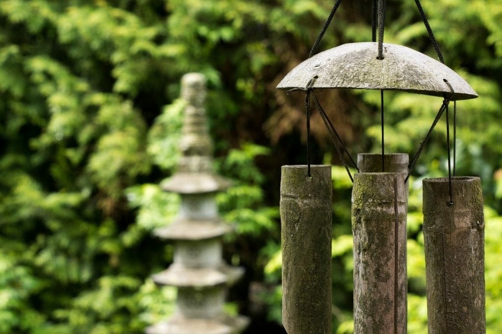 Bamboo wind chimes hanging in a lush garden with a stone pagoda in the blurred background and a self-storage unit subtly integrated into the scenery.