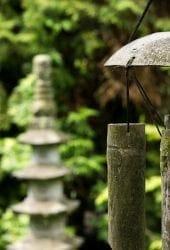 Bamboo wind chimes hanging in a lush garden with a stone pagoda in the blurred background and a self-storage unit subtly integrated into the scenery.