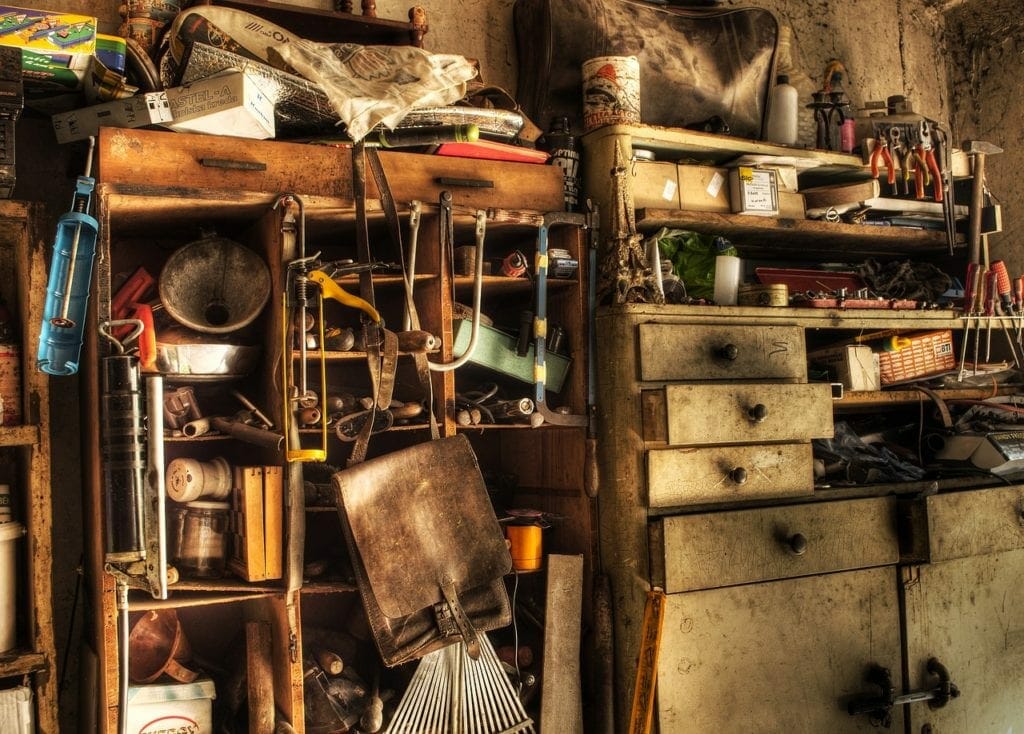 A cluttered workshop with various tools, drawers, and old furniture designated for self storage bathed in warm light.