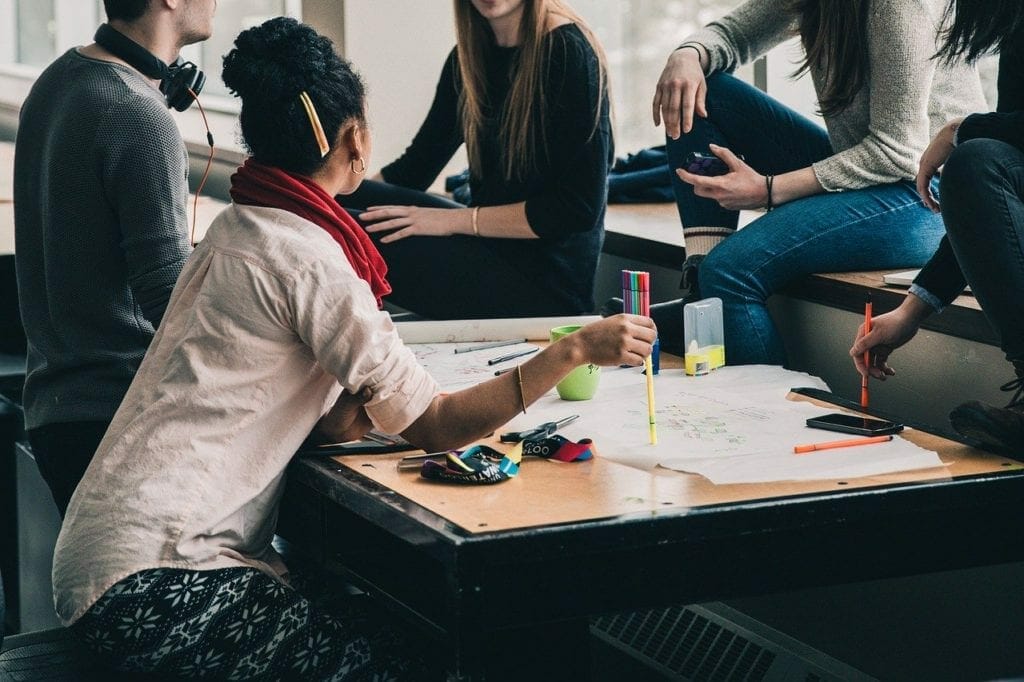Group of young adults engaged in a discussion around a table scattered with papers and colorful markers, planning the layout for a self storage unit.