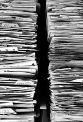 Black and white image of two densely packed piles of documents and files, showing visible labels with dates and codes, ideal for storing in self storage.